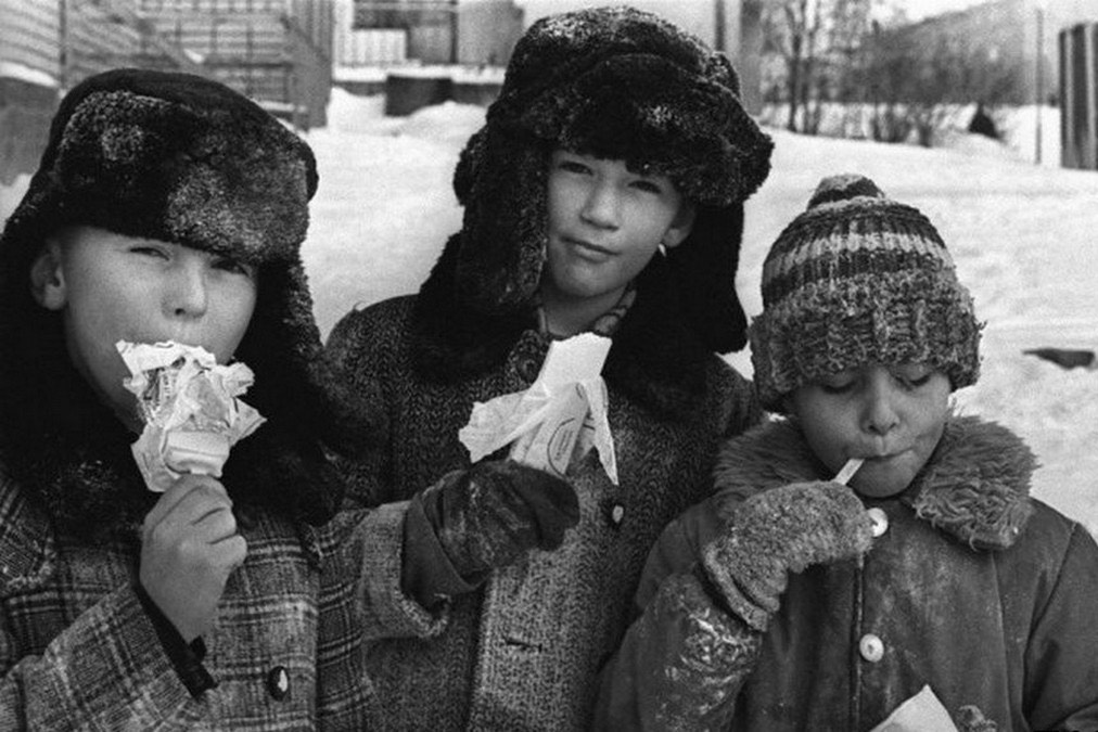 Black & white vintage photo of 3 boys in winter gear, eating bananas.